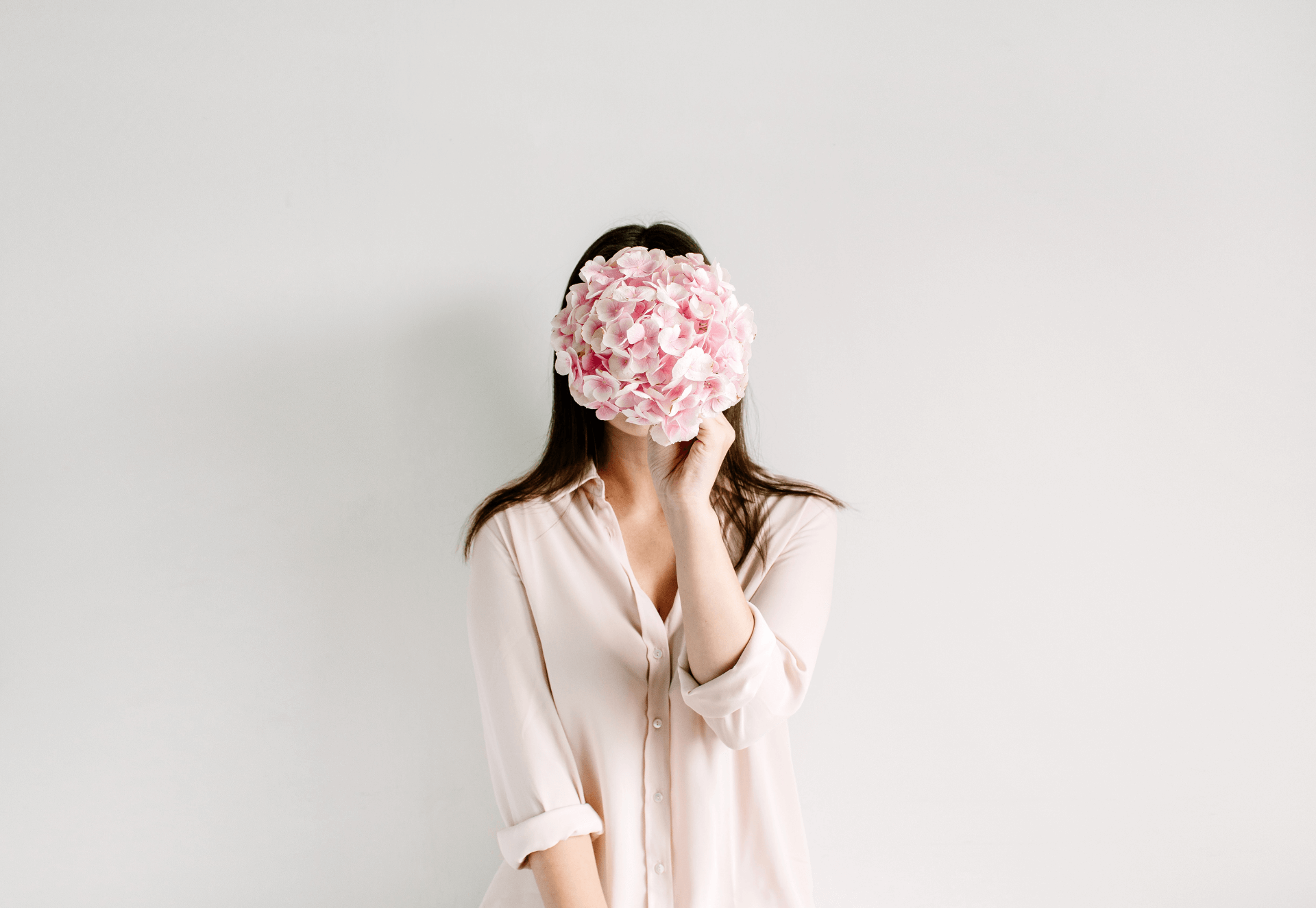 Image of a woman holding a large pink hydrangea slower over her face.