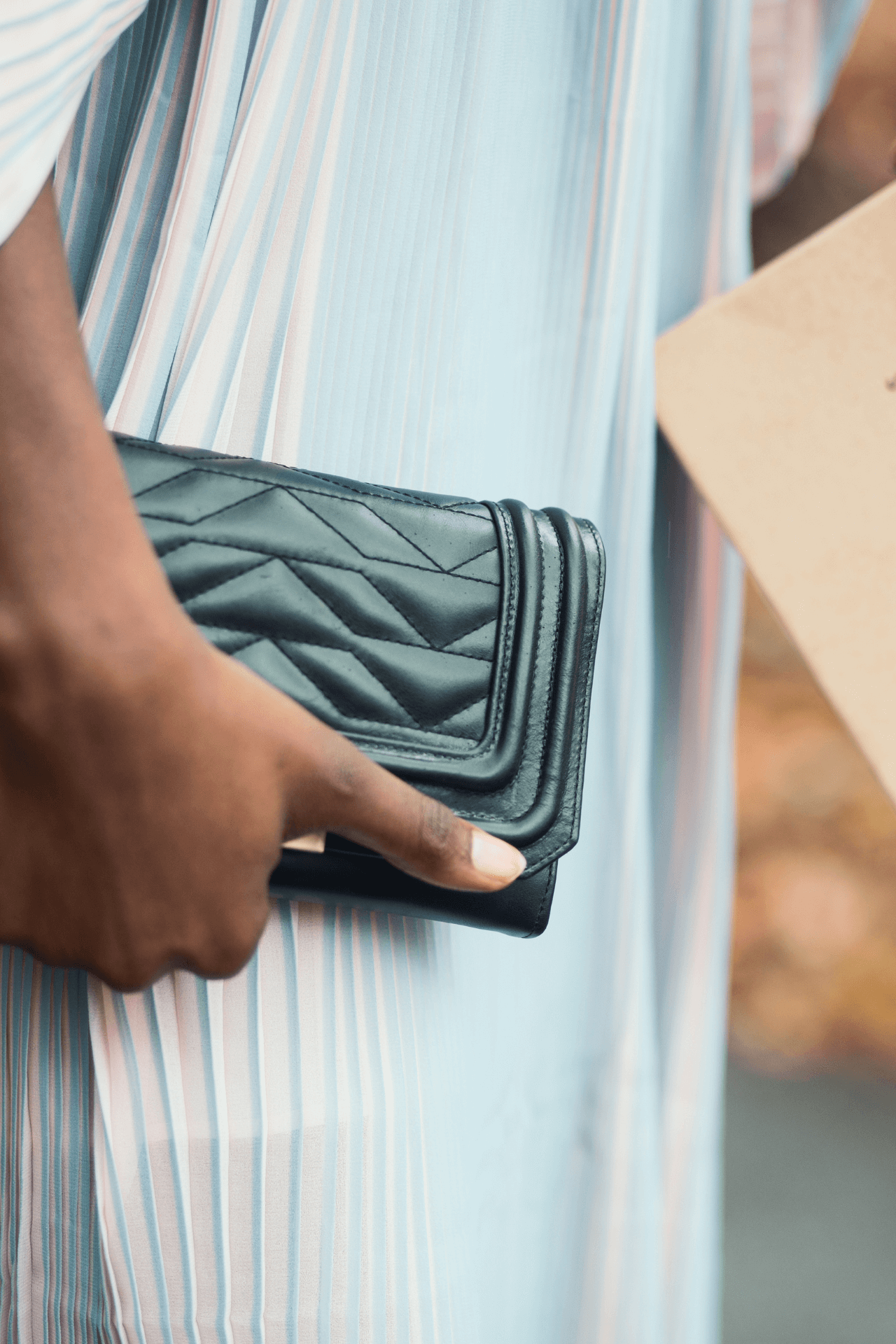 image of a persons hand holding a quilted leather clutch bag and wearing a pleated dress.