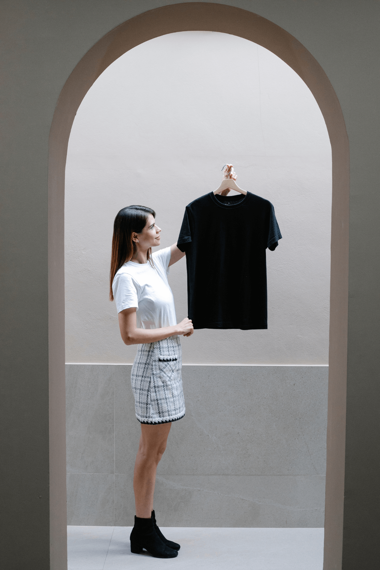 Image of a woman holding up a black t shirt under an arched doorway