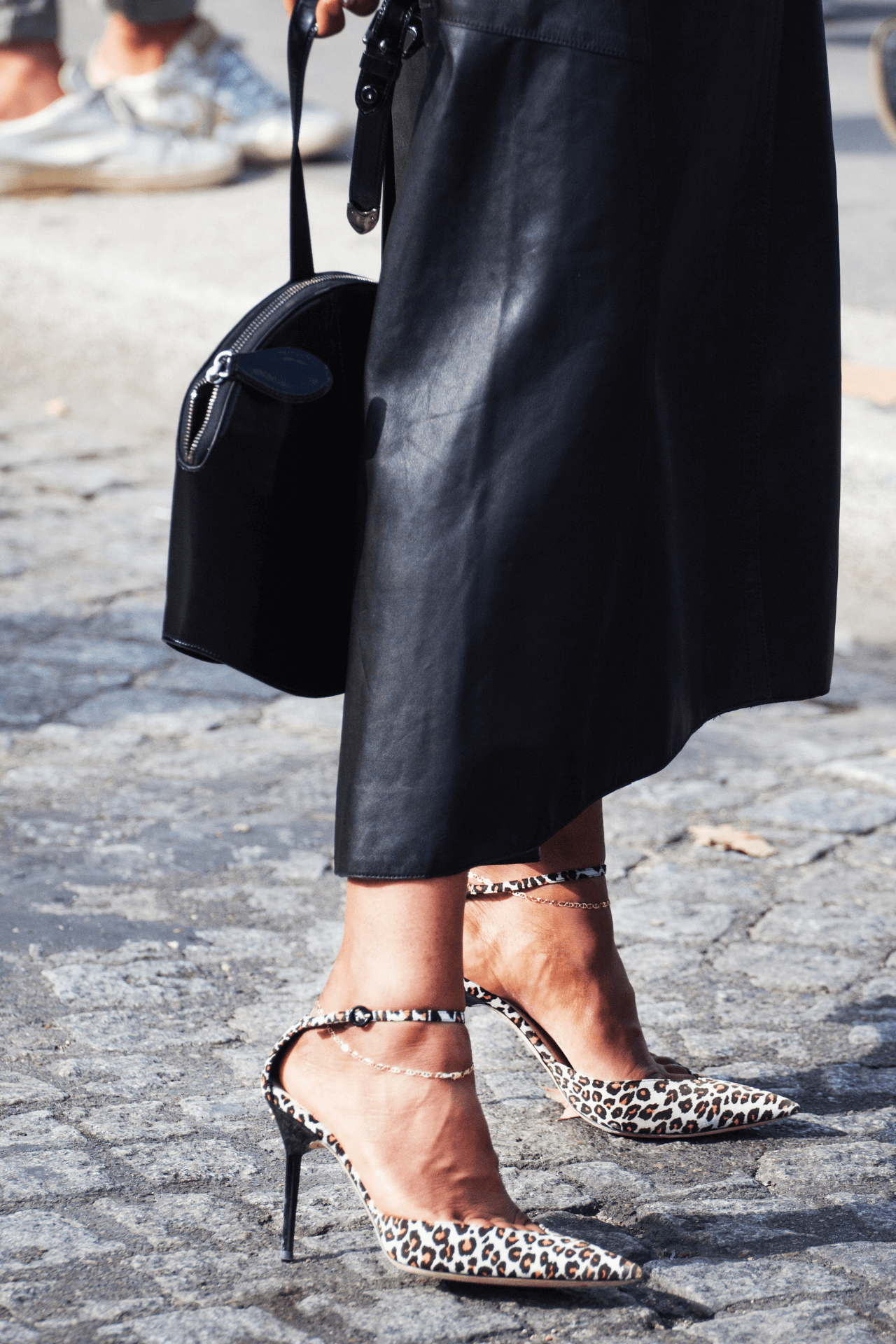 image of a persons legs wearing a black leather skirt and heeled leopard print shoes and black leather bag