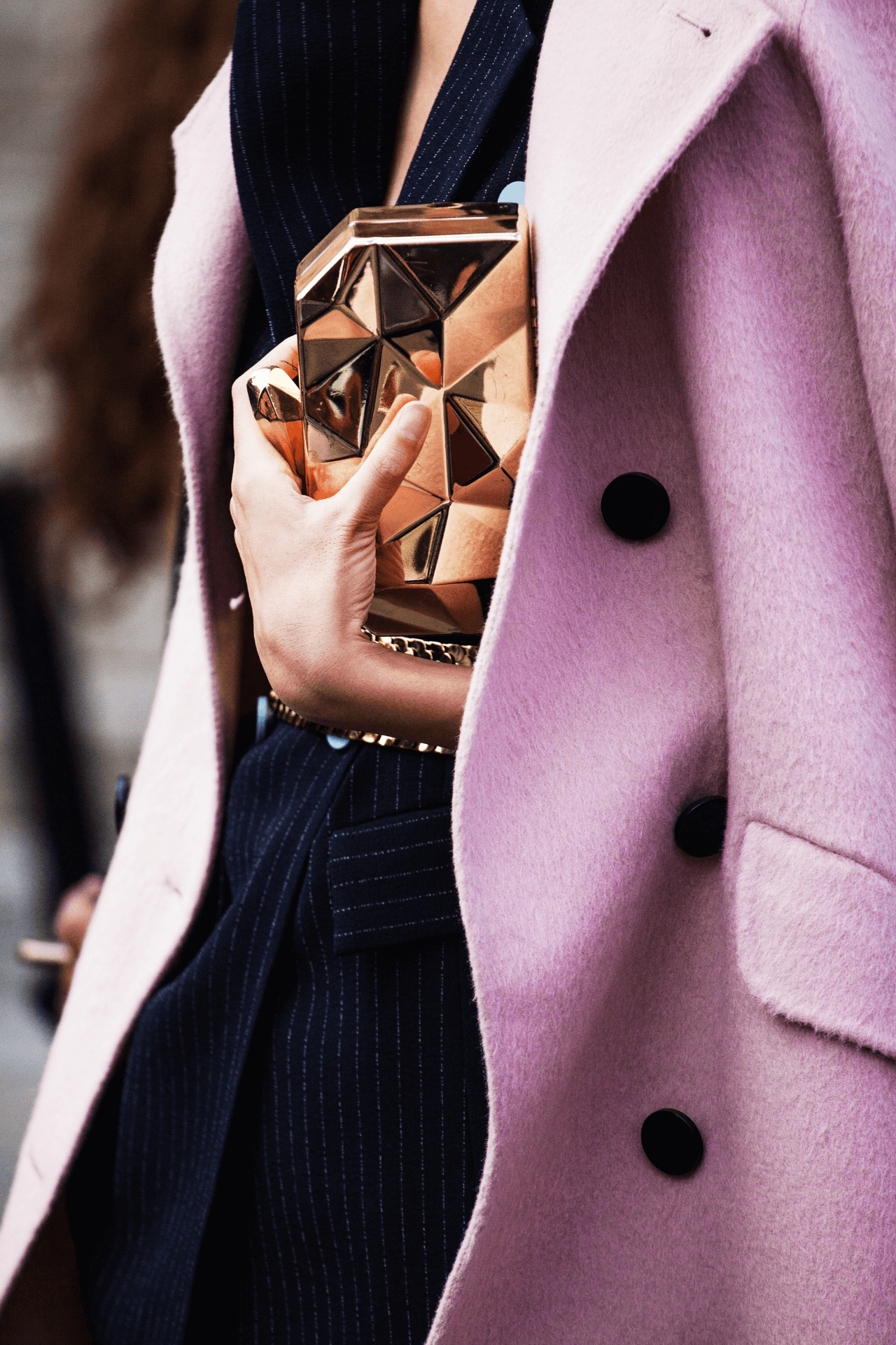 Close up image of a fashionable pink wool coat draped over shoulders with an arm around a texture golden clutch. 