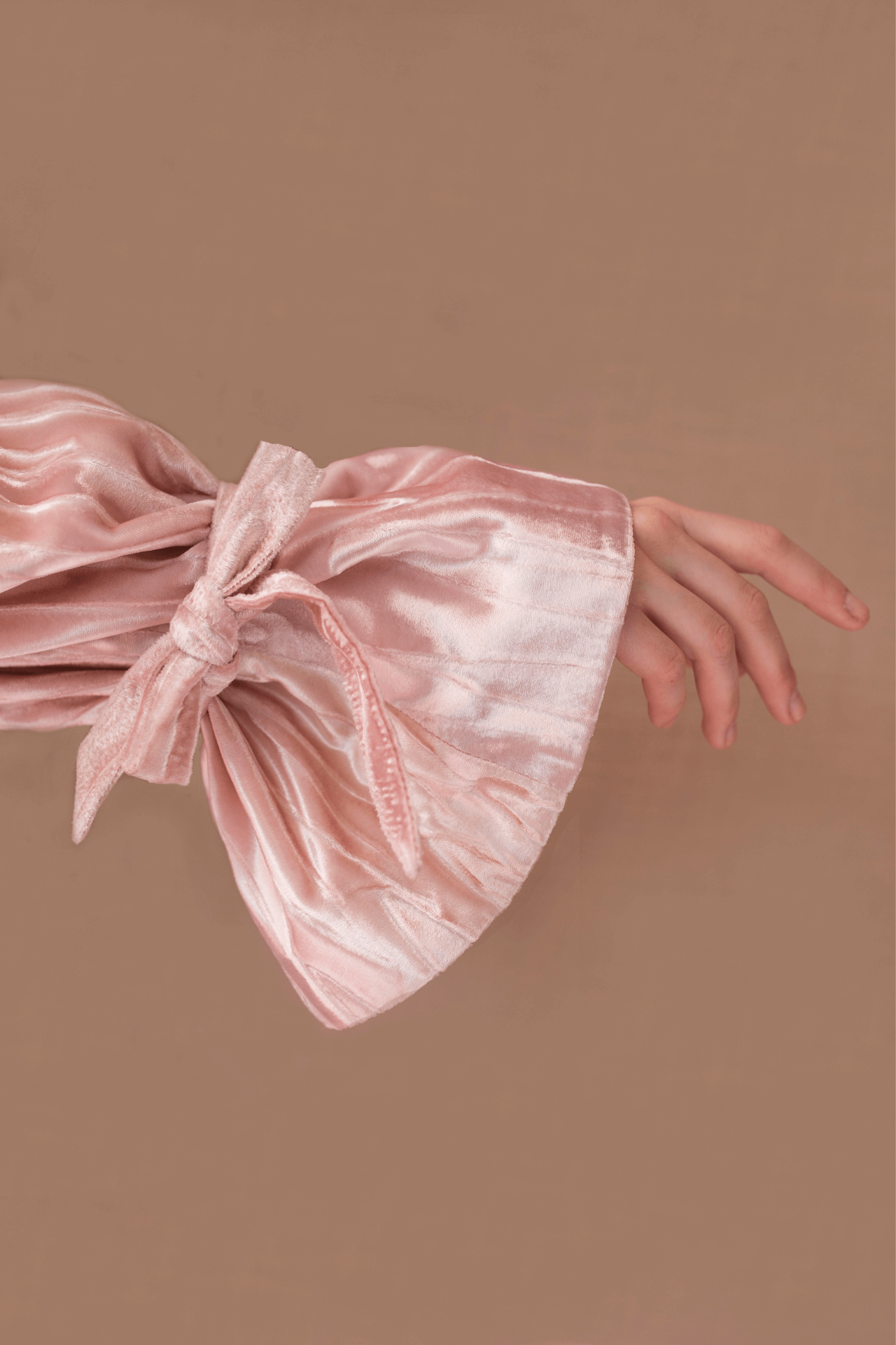 Image of a a bell sleeve pink velvet top with a ribbon tie and a hand reaching into the centre of the frame.